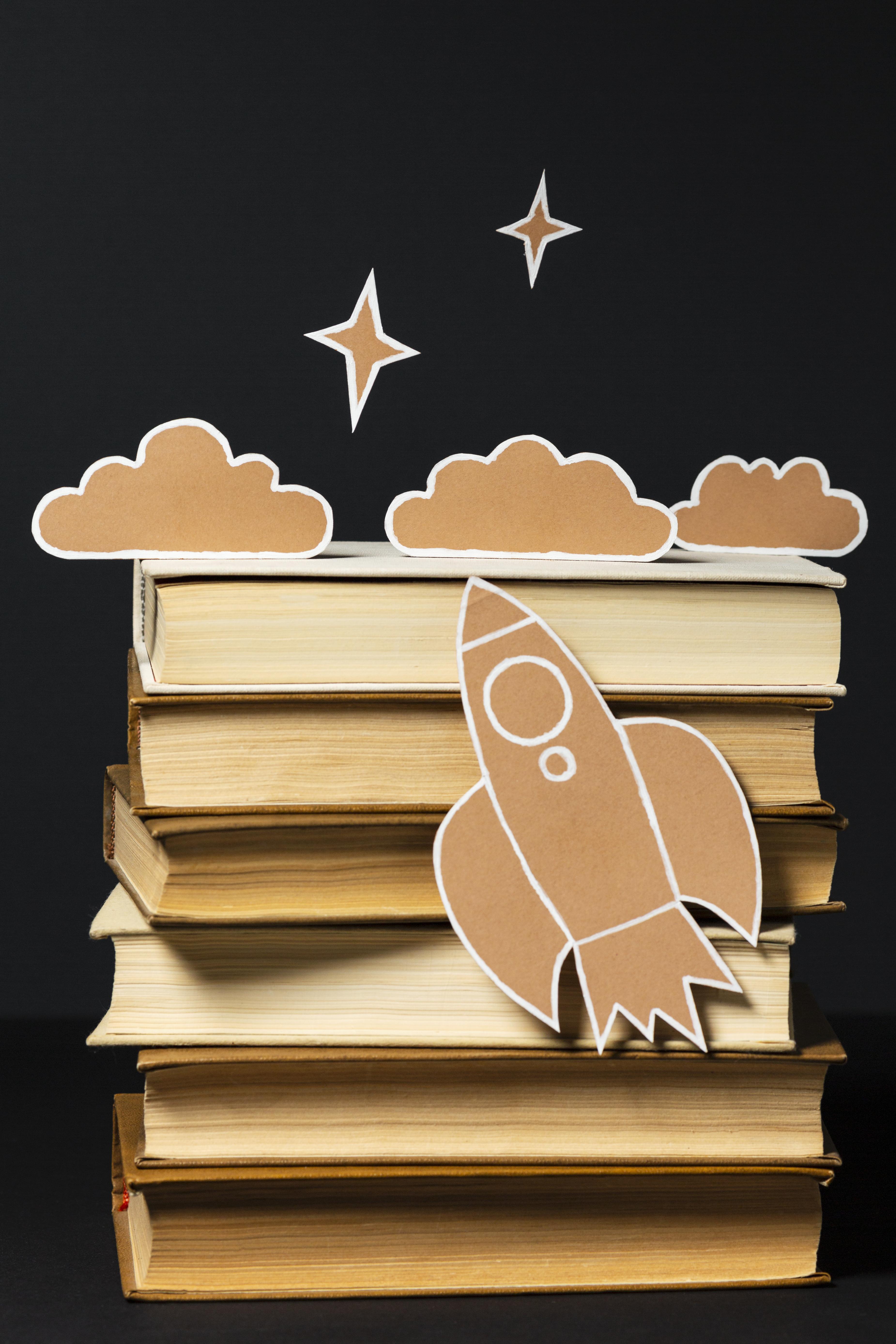 Eine Rakete aus Karton fliegt Richtung Karton-Himmel an einem Bücherstapel entlang.