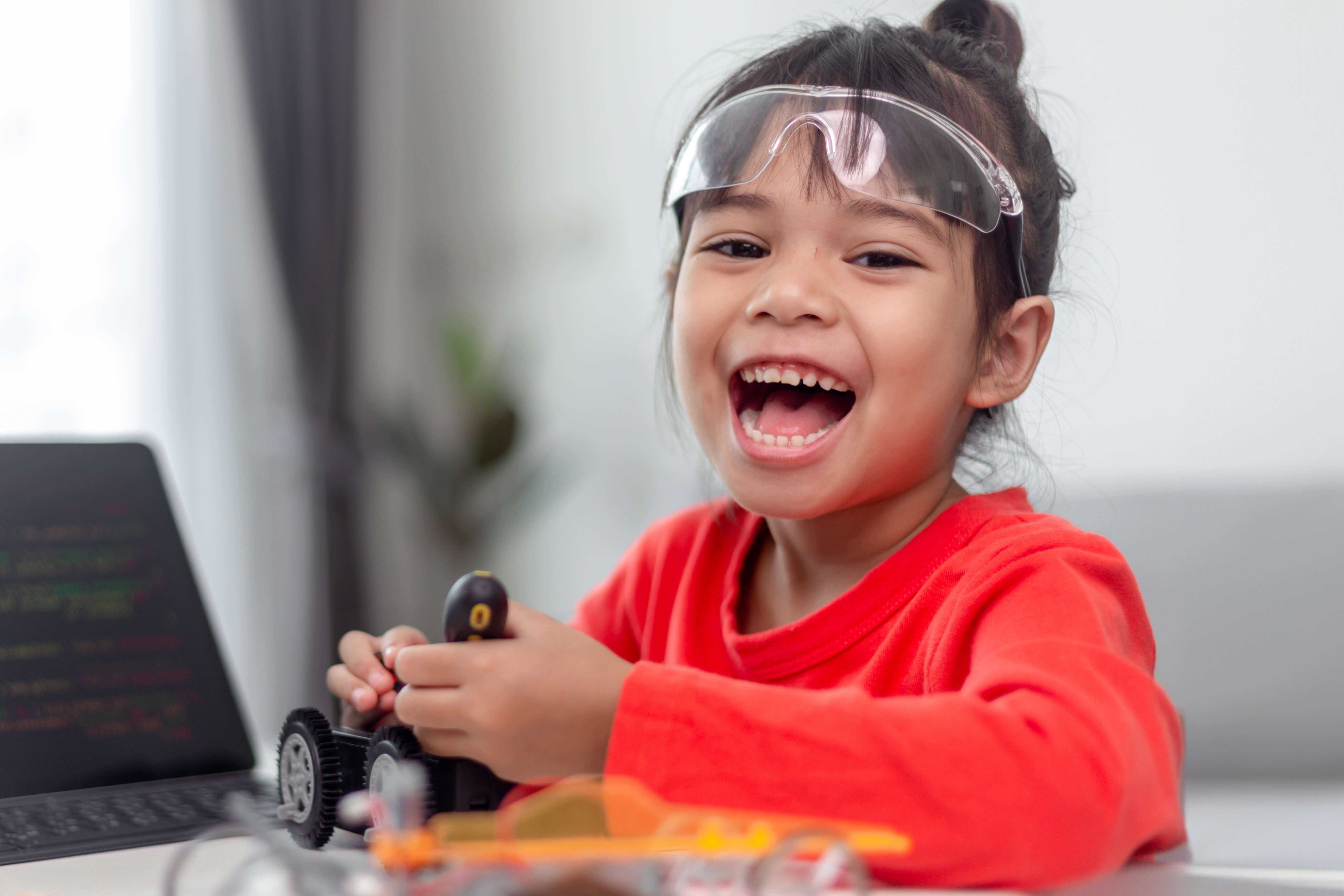 Kind baut fröhlich einen kleinen Roboter und hat einen Computer zur Hilfe daneben.