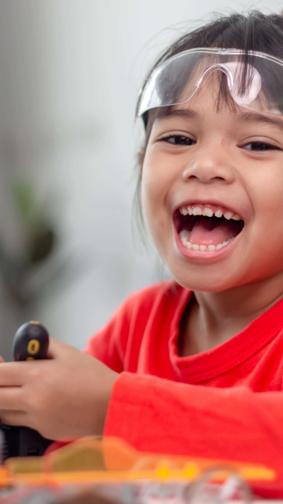 Kind baut fröhlich einen kleinen Roboter und hat einen Computer zur Hilfe daneben.