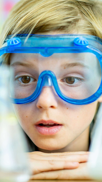Kind mit Schutzbrille, das sich Reagenzgläser im Labor ansieht.