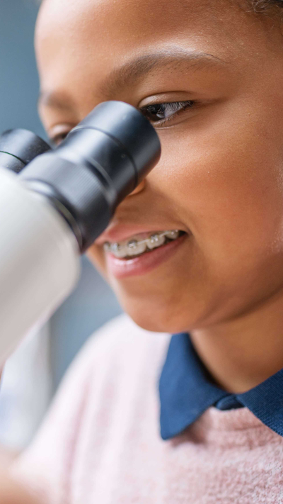 Mädchen, das etwas durch ein Mikroskop betrachtet.