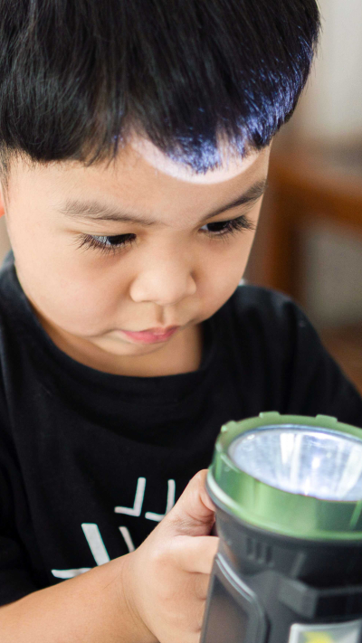 Junge, der mit einer Taschenlampe spielt.