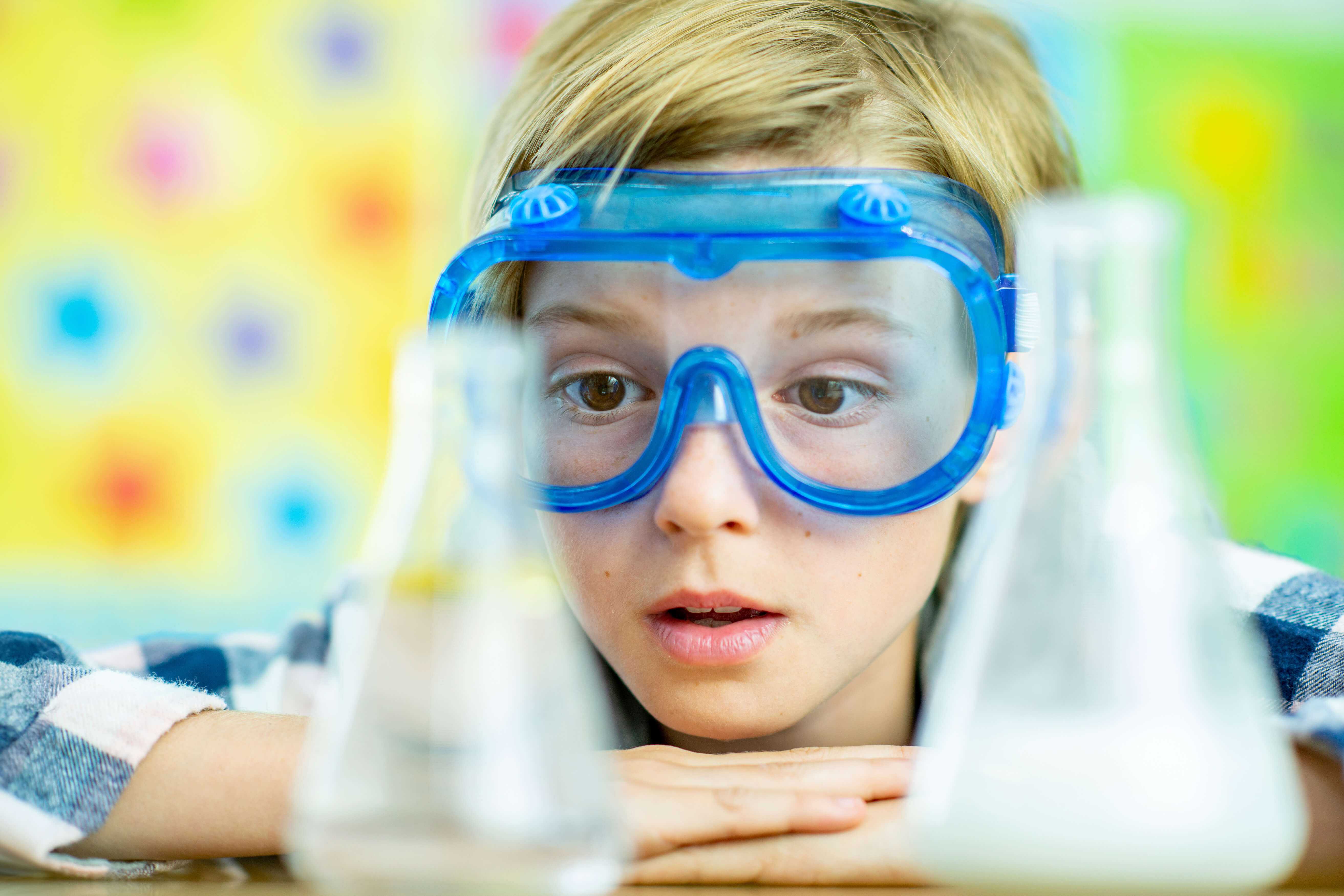 Kind mit Schutzbrille, das sich Reagenzgläser im Labor ansieht.