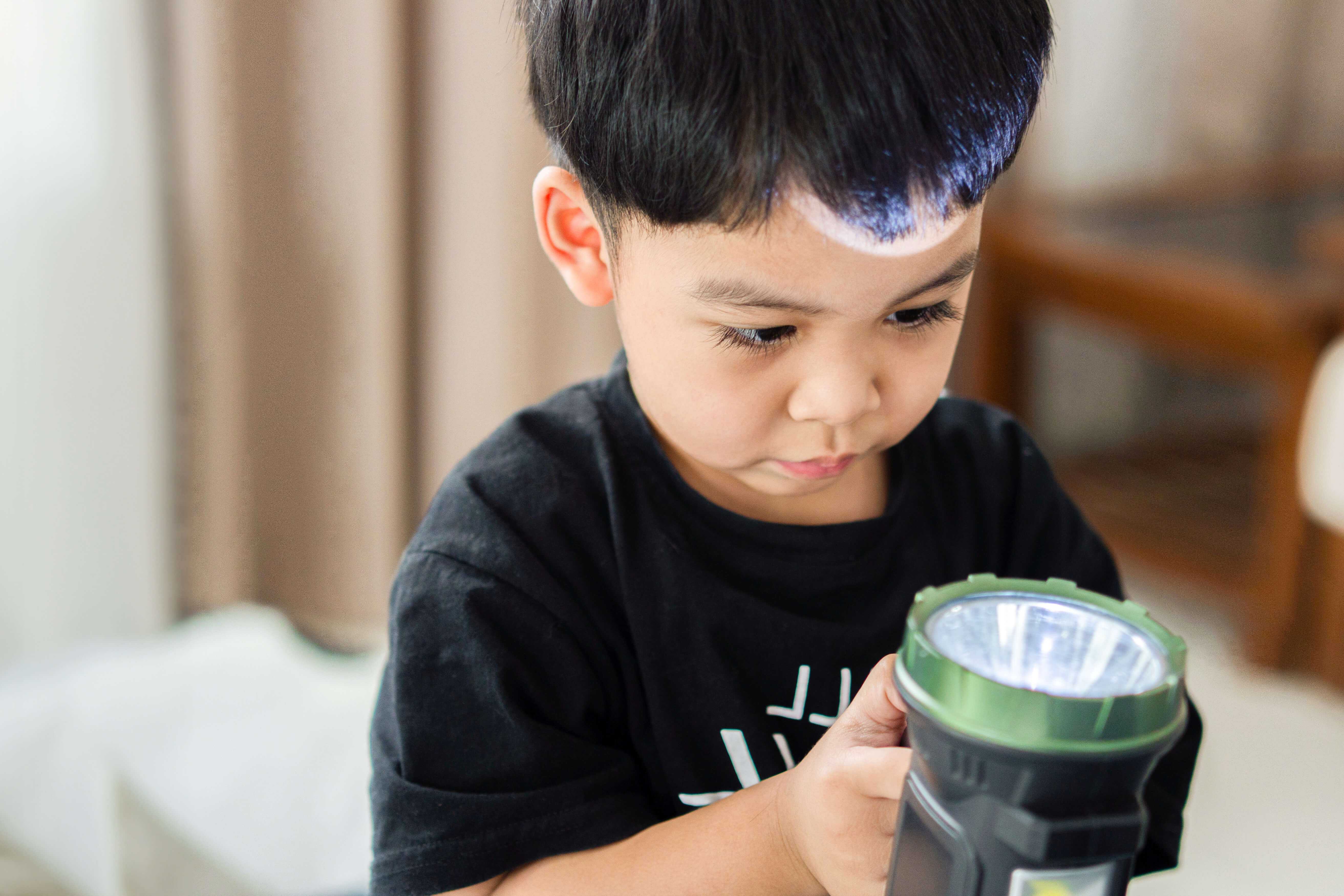 Junge, der mit einer Taschenlampe spielt.