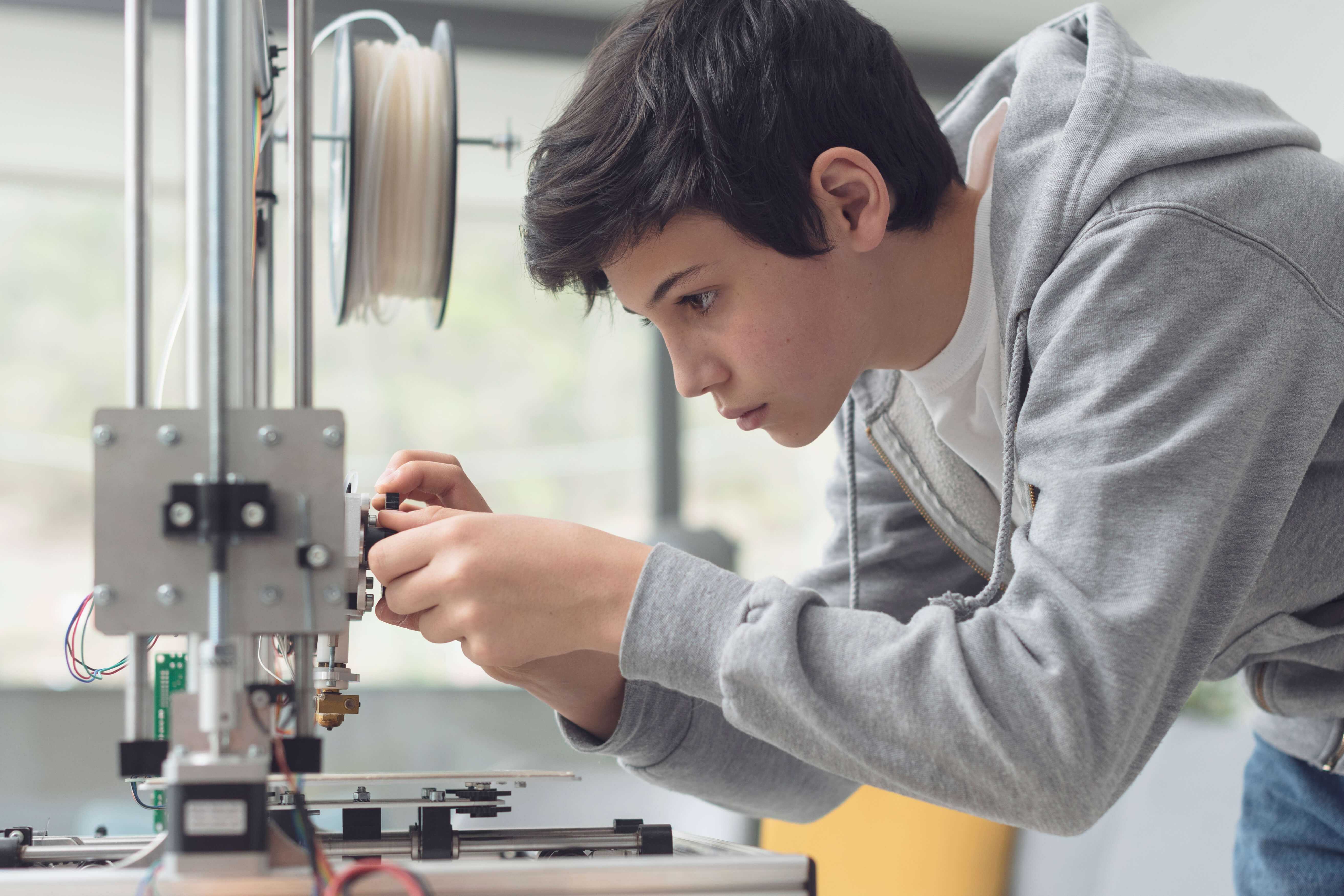 Junge, der einen 3D Drucker einstellt.