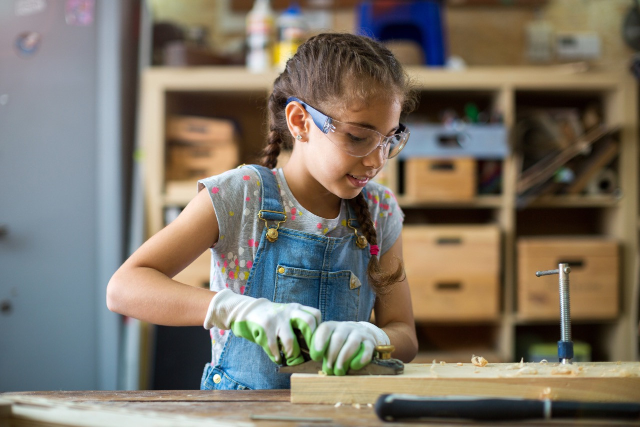 Mädchen, das in einer Werkstatt ein Holzstück hobelt.