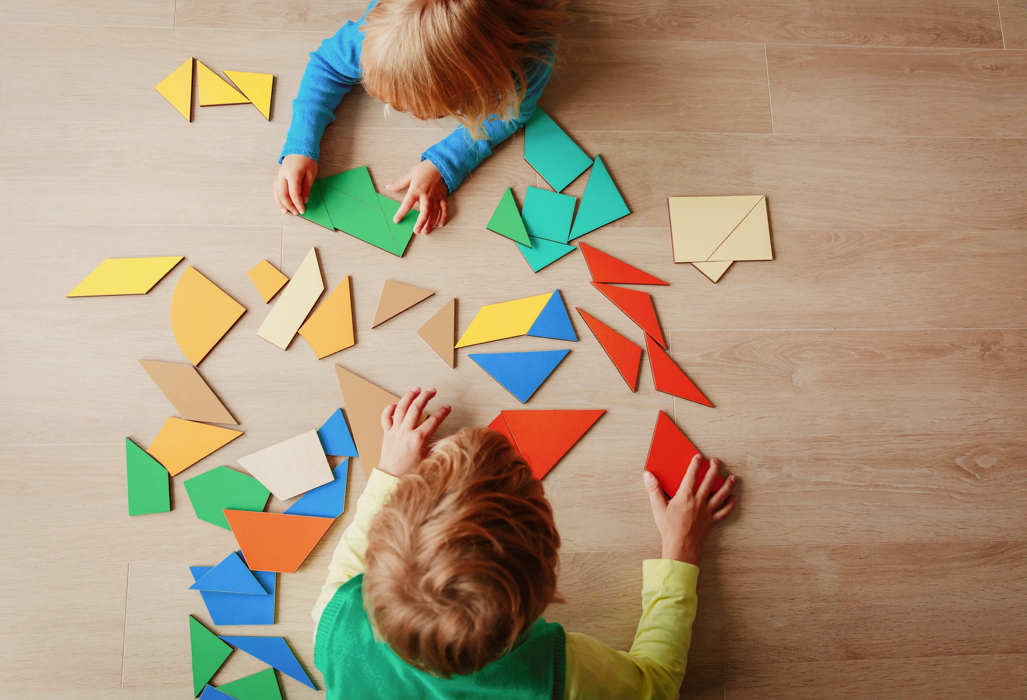 Zwei Kinder schieben Tangram-Puzzleteile auf einem Tisch herum.