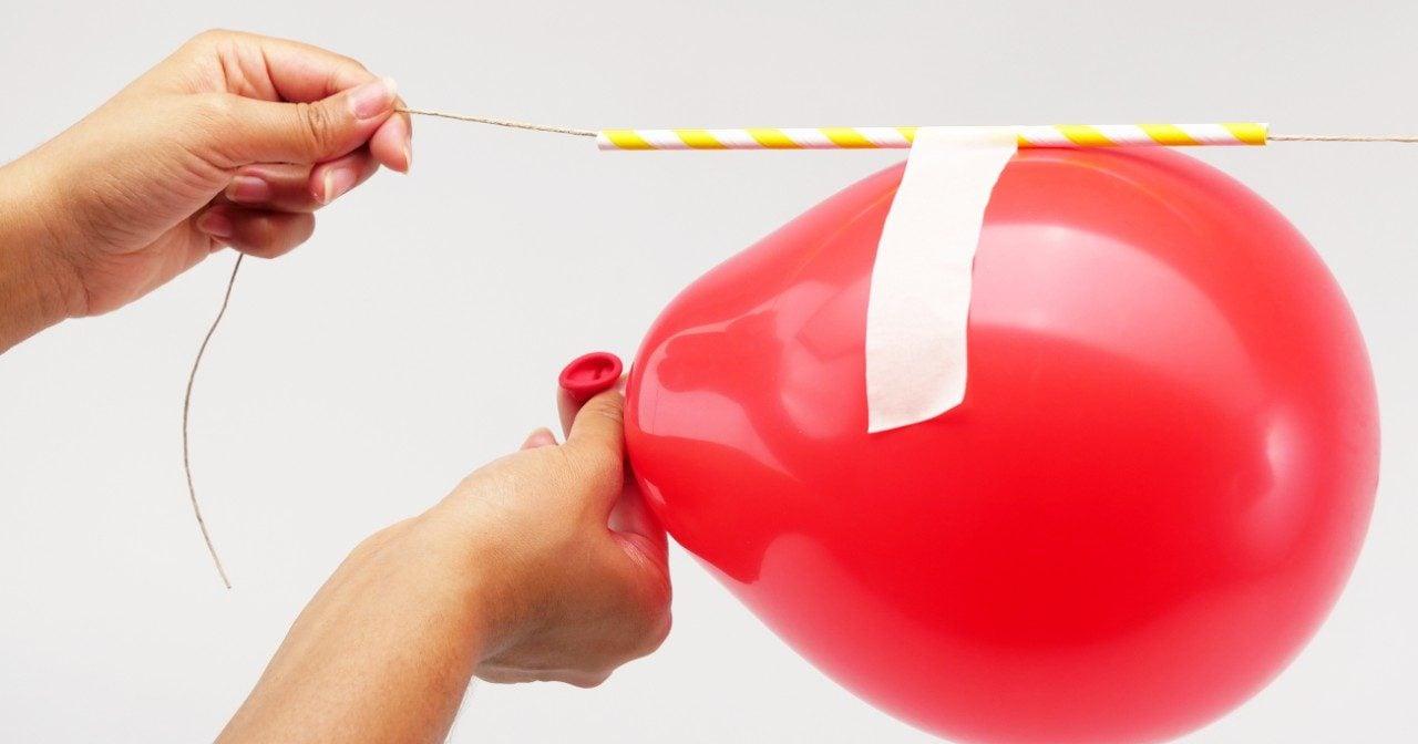 Experiment mit einem roten Ballon, der durch einen Strohhalm an einer Schnur hängt.