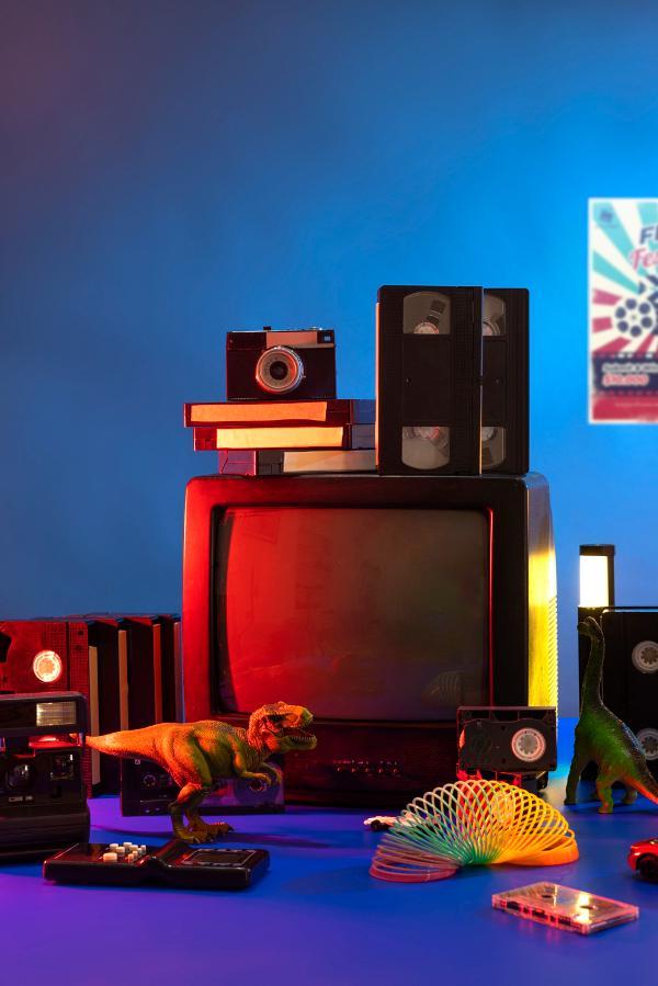 Ein alter Fernseher mit Videokassetten, Kamera und Spielzeug-Dinosauriern im bunten Licht.